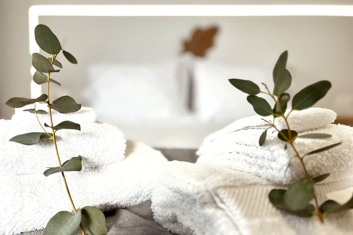 A neatly arranged set of white towels with a plant branch in the foreground, placed on a textured surface.
