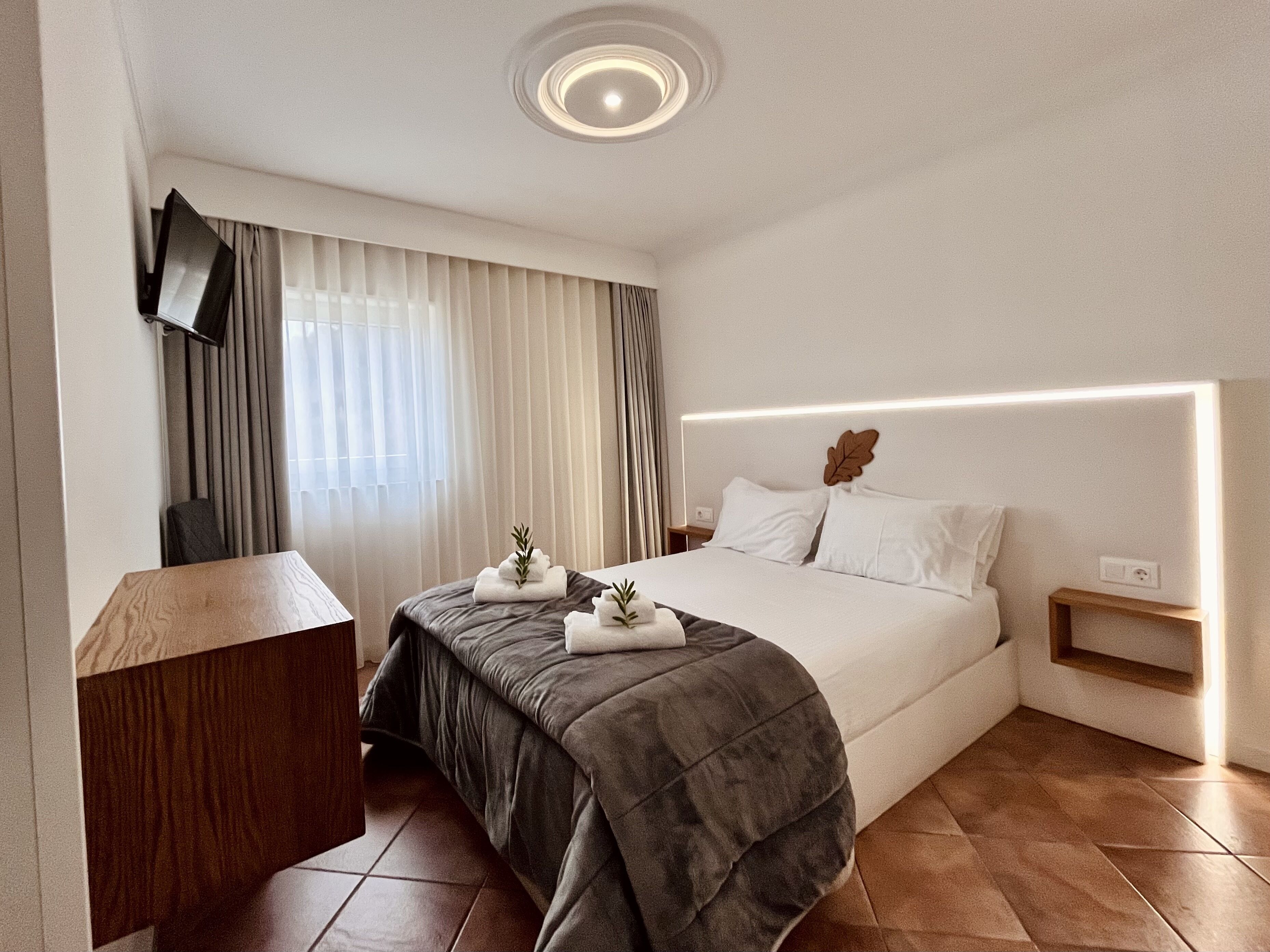 Una habitación de hotel moderna con una cama grande, un escritorio y un televisor instalado en la pared.