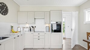 Une cuisine moderne avec des meubles blancs, un four encastré et une horloge au mur.