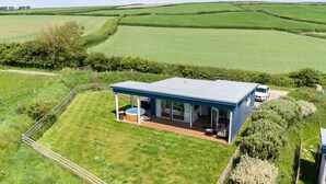 Une maison moderne dotée d’une grande terrasse, d’un jacuzzi et d’une voiture garée à proximité.
