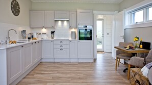 Une cuisine moderne avec des meubles blancs, un four encastré et un coin repas comprenant une table et des chaises.