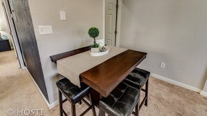 A dining area with a wooden table, two black leather benches, a small potted plant, and a door in the background.