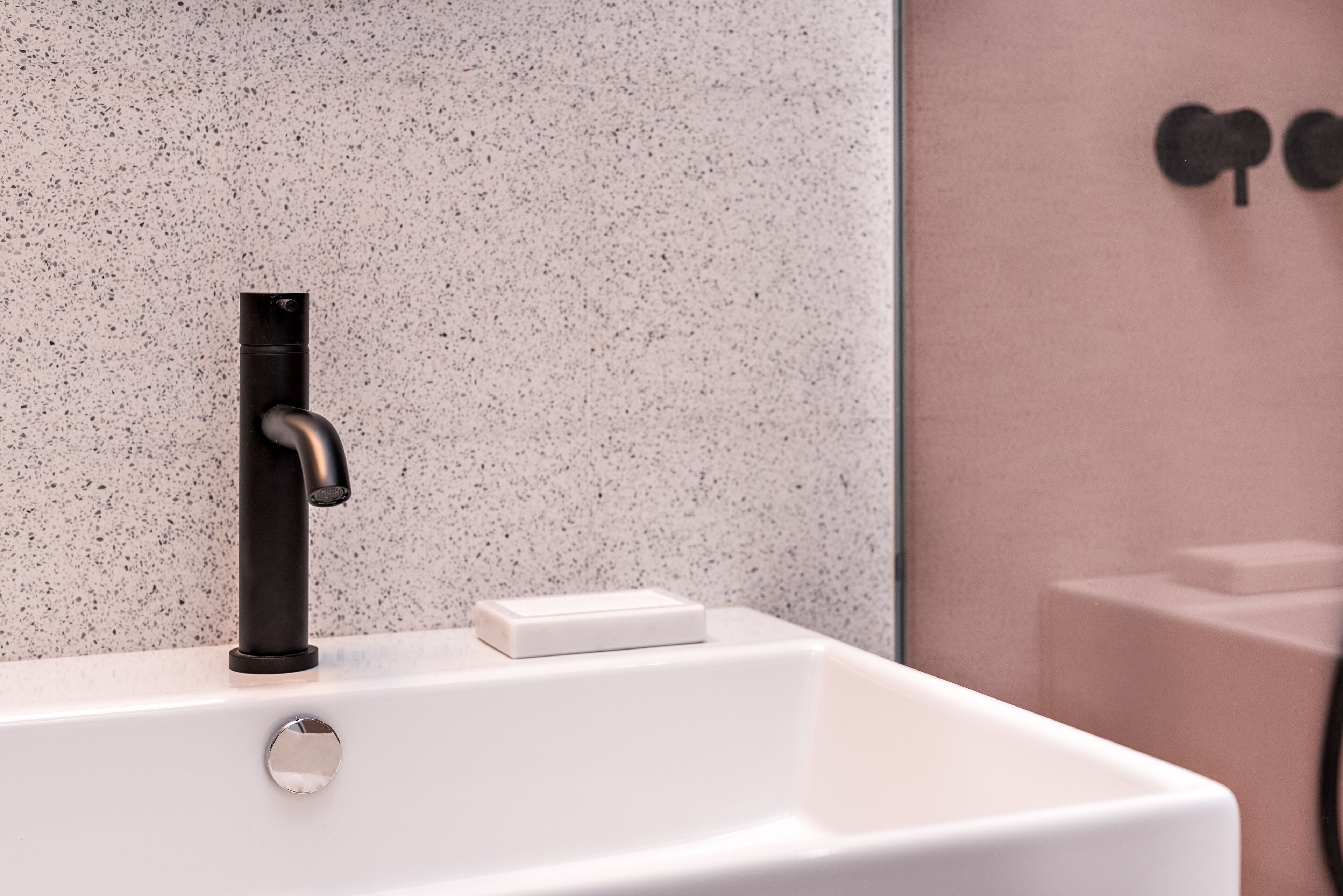 A bathroom with a white sink, a black faucet, and a soap dish.