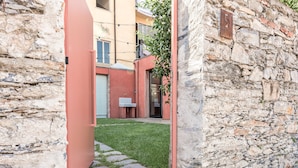 Un muro de piedra con un letrero con el número '5', una puerta roja y un pequeño césped con piedras para caminar.