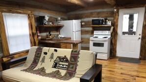 A cozy log cabin room with a bed, a kitchenette, a white refrigerator, a stove, and a door with a window.