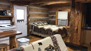 A log cabin interior with a bed, a small kitchenette, and a window.