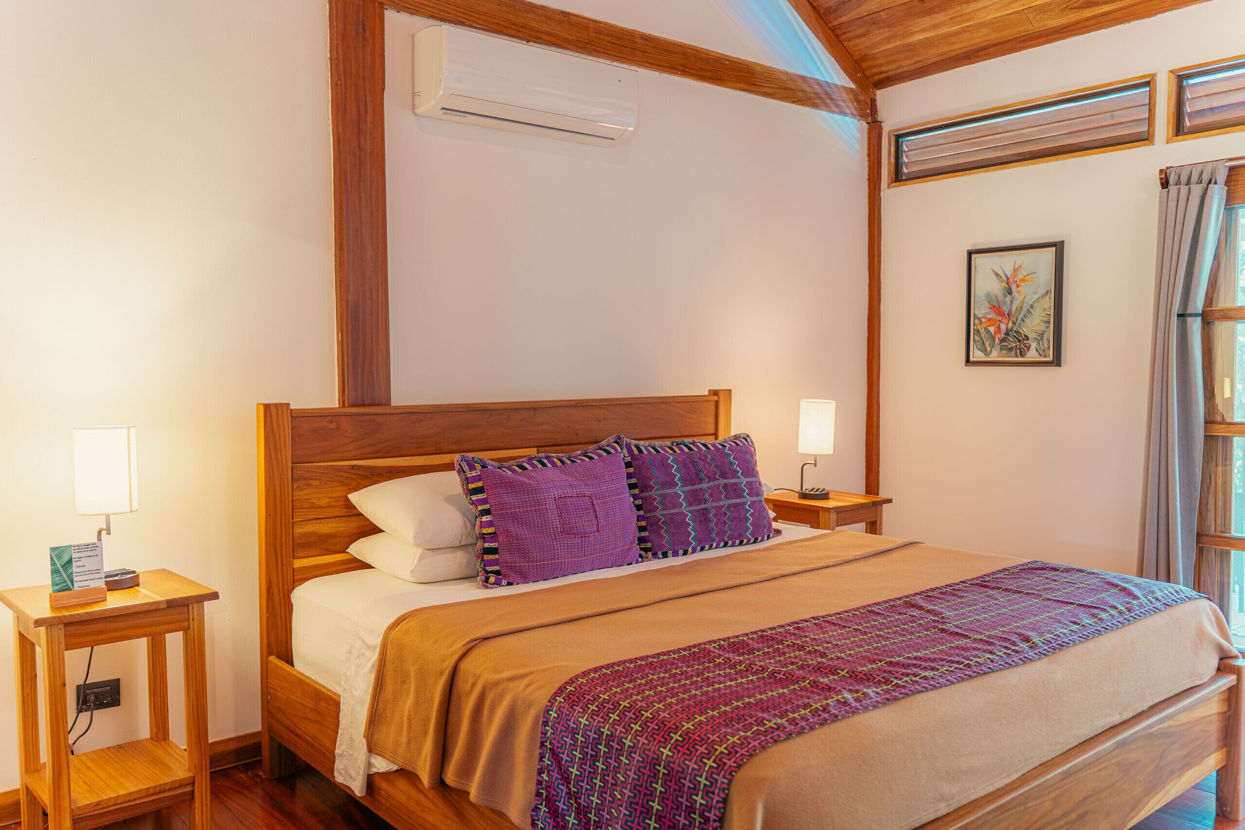 Een slaapkamer met een houten bed, twee nachtkastjes, een wandairconditioner en een raam met gordijnen.