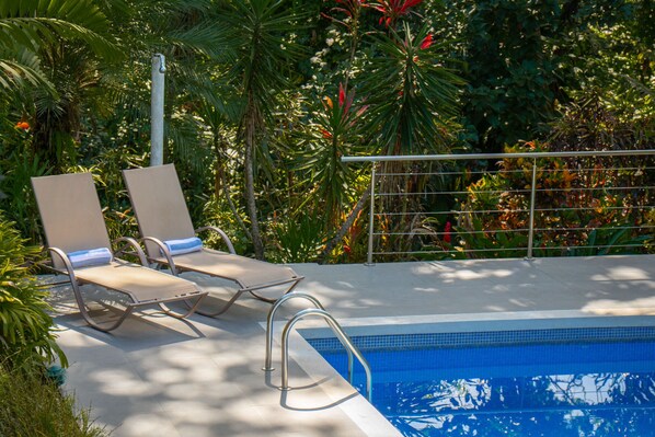 Zona junto a la piscina con dos sillas de descanso y una barandilla metálica.