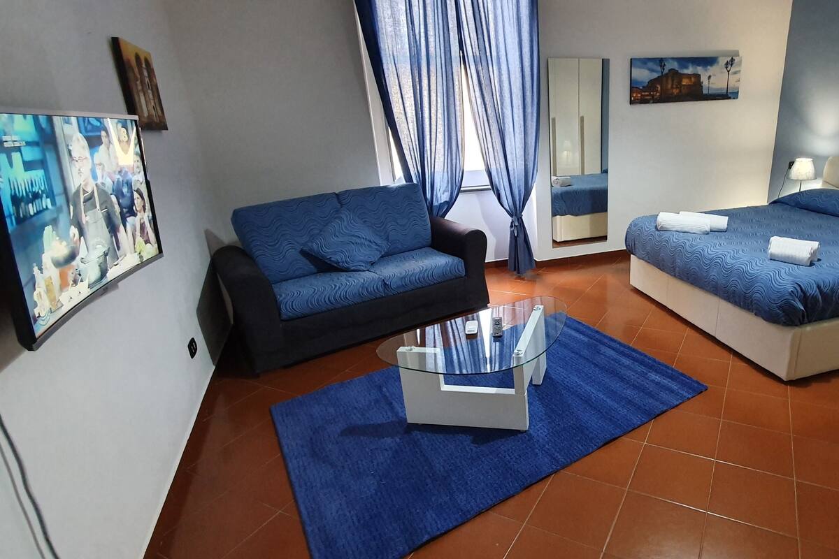 A hotel room with a bed, a sofa, a small table, and a TV.