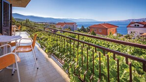 Un balcon avec vue sur la mer et les montagnes, comprenant une table et des chaises.