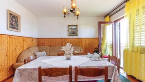 Un coin repas avec un mur lambrissé en bois, une table recouverte d’une nappe blanche, un lustre et un rideau jaune.