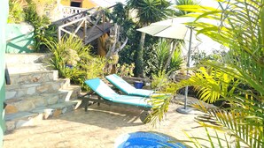 A pool area with two lounge chairs, a small pool, and a staircase leading to a building.