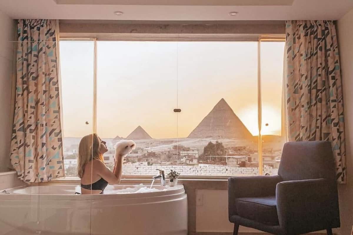 A modern living room with a large window offering a view of the pyramids at sunset.