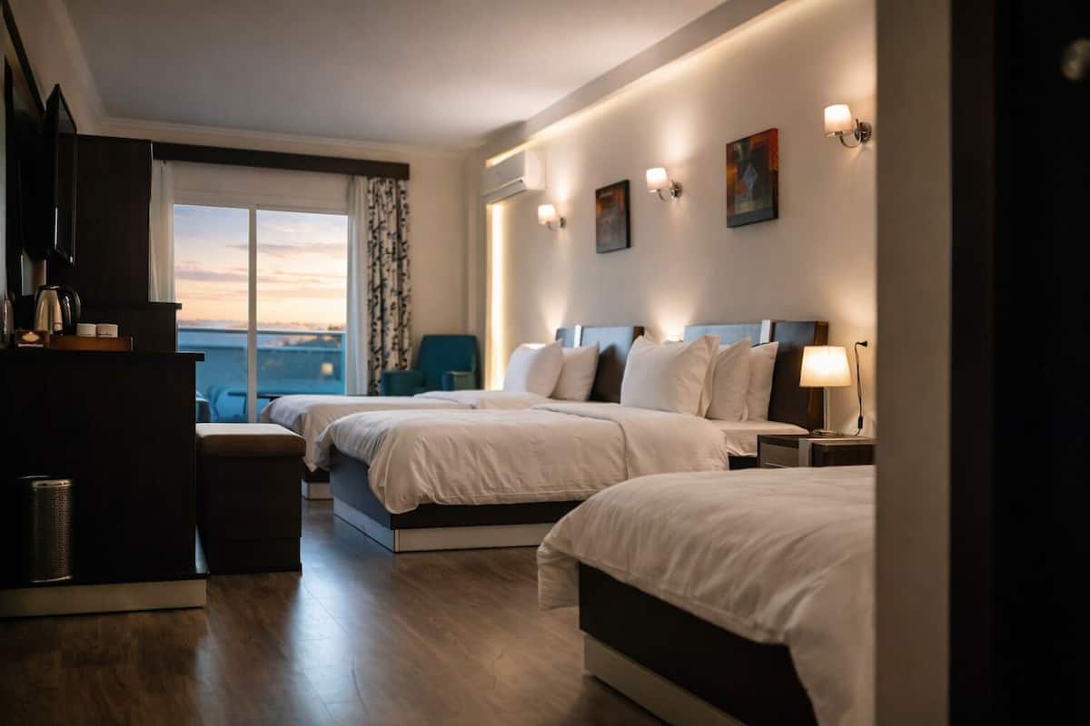 A hotel room with two beds, a desk, a chair, and a view of the city.