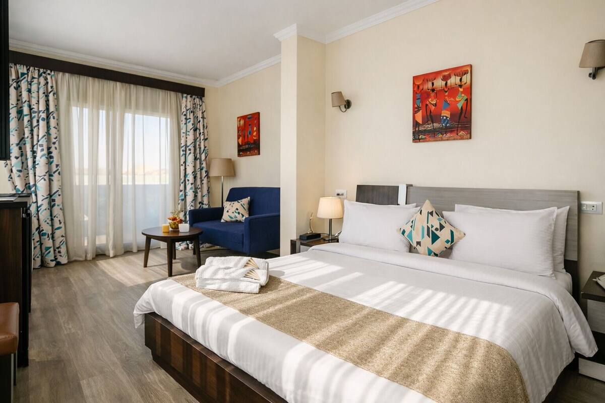 A hotel room with a bed, a blue armchair, a small table, and a lamp.