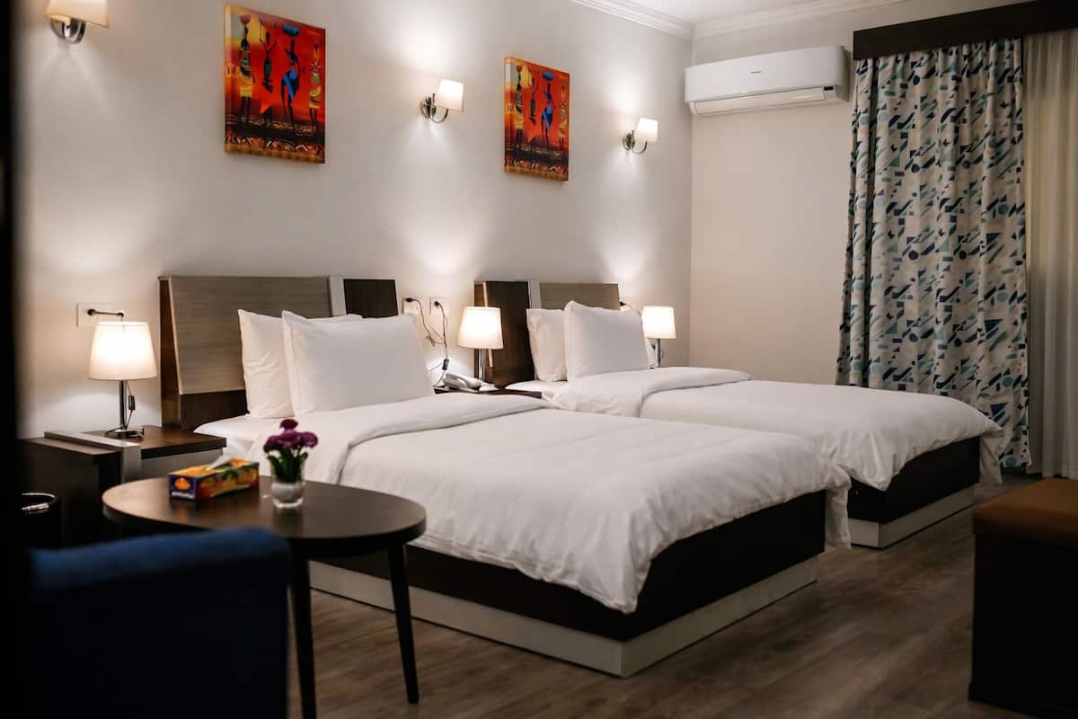 A hotel room with two beds, a round table, a nightstand, and artwork on the walls.