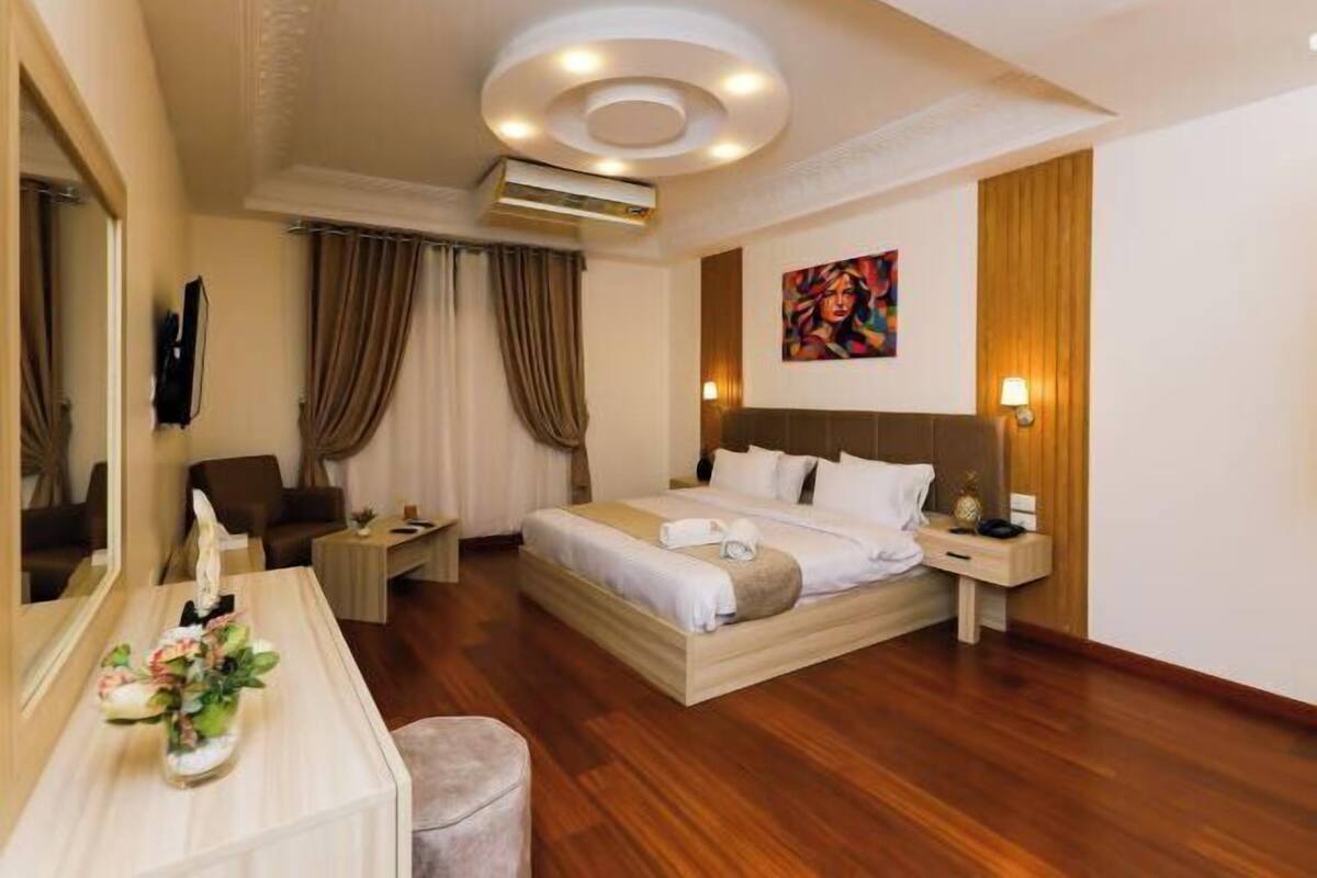 A hotel room with a bed, bedside table, lamp, and a painting on the wall.