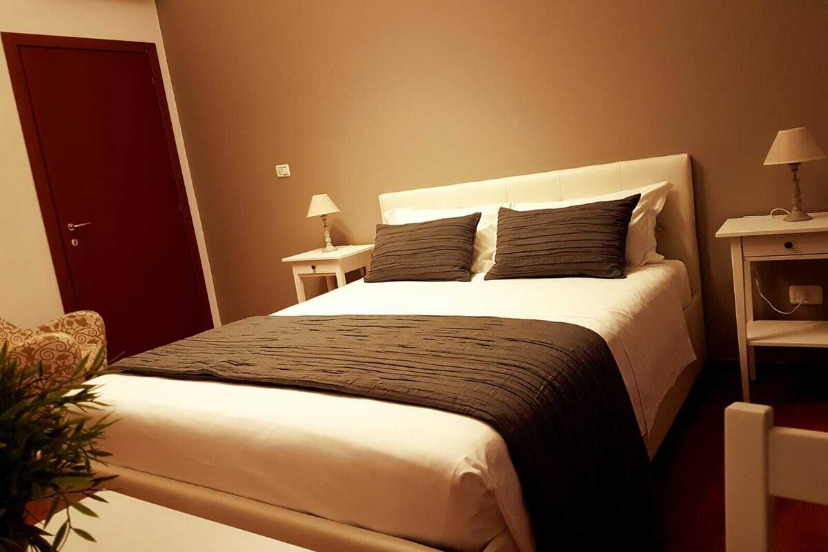 A hotel room with a bed, bedside tables, a lamp, and a door.