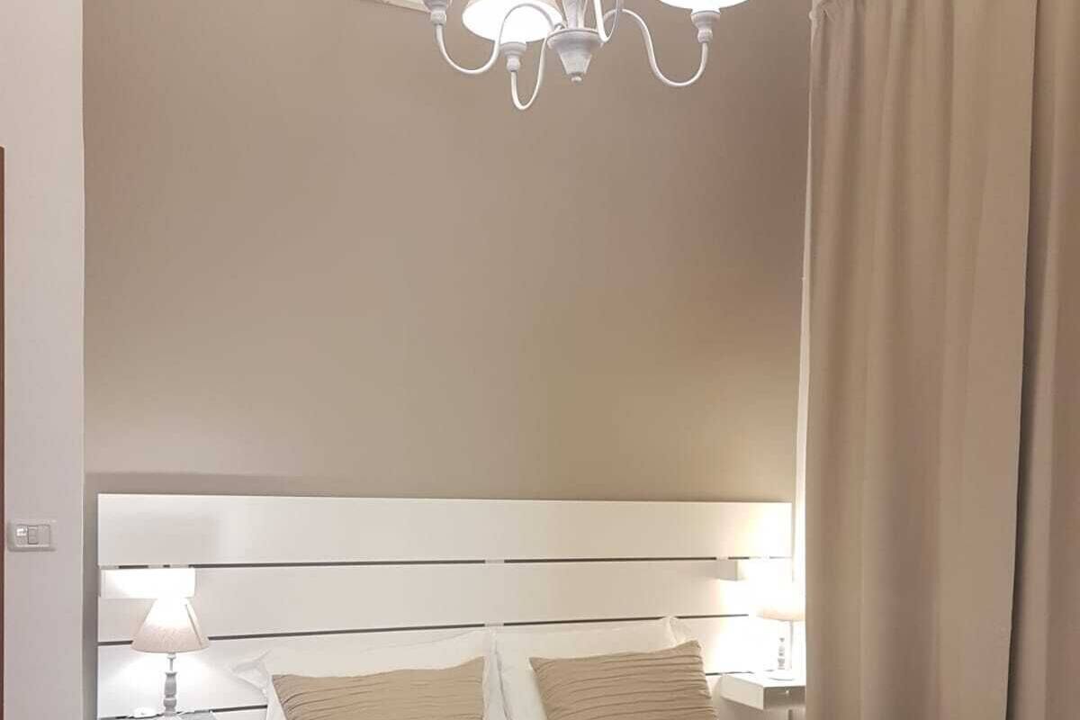 A hotel room with a large bed, a white headboard, a bedside table with a lamp, and a chandelier.