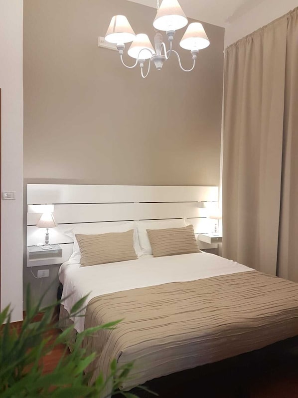 Habitación de hotel con una cama grande, cabecera blanca, mesita de noche con lámpara y candelabro.