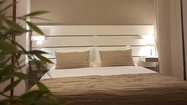 Une chambre d’hôtel avec un lit, des lampes de chevet, un lustre et une plante.