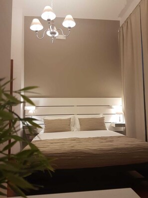 Una habitación de hotel con cama, lámparas de noche, candelabro y una planta.