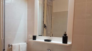 Une salle de bain avec un lavabo blanc, un miroir, un porte-serviettes et une poubelle.