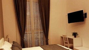Une chambre d’hôtel équipée d’un lit, d’un bureau, d’une chaise, d’un téléviseur fixé au mur et d’une fenêtre avec des rideaux.