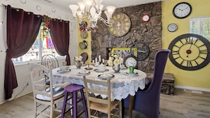 Comedor con una mesa dispuesta para cuatro personas, sillas, una lámpara de araña y relojes de pared decorativos.