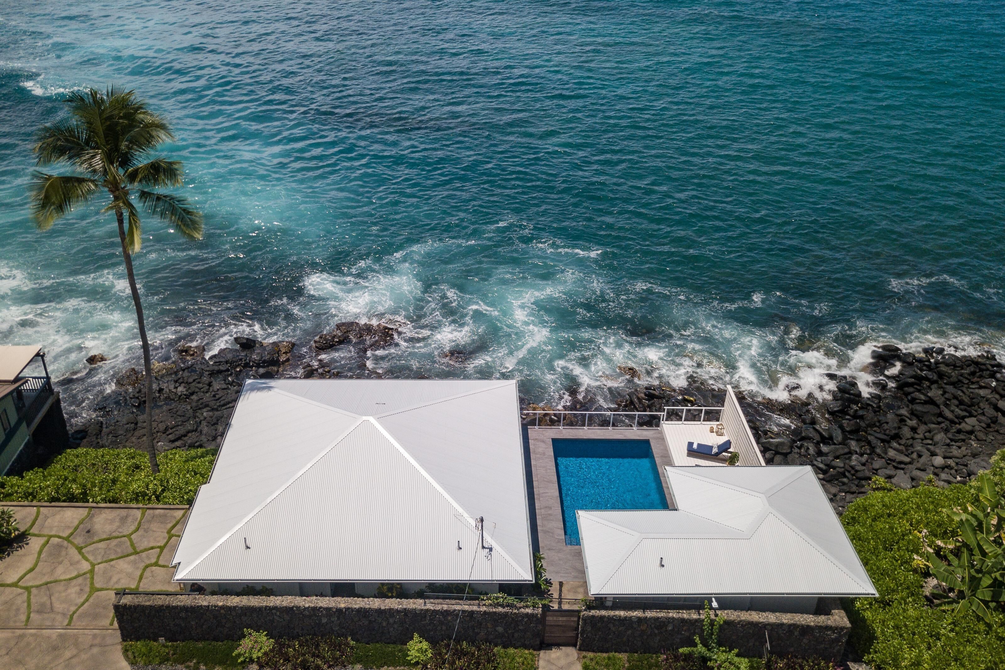 A coastal property with a swimming pool, a white-roofed building, and a palm tree.