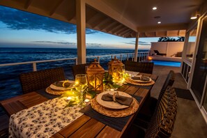 Uma sala de jantar com vista para o oceano, com uma mesa de madeira posta com pratos, copos e velas.