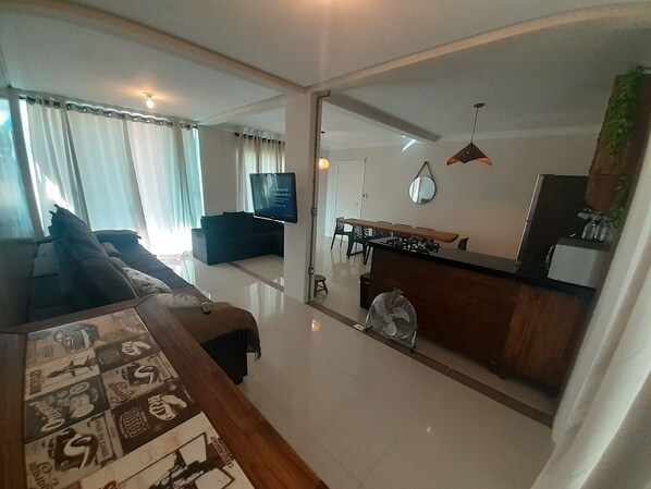 A modern living room with a sofa, a coffee table, and a TV. There is a dining area with a table and chairs.