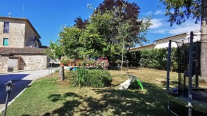 A stone building with a tiled roof, a grassy yard with a tree, and a playground with a slide.