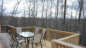 Eine Holzterrasse mit Tisch und Stühlen, umgeben von einem Geländer, mit Blick auf einen bewaldeten Bereich.