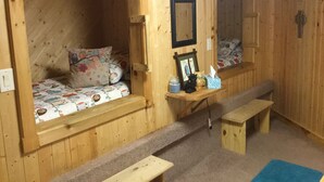 Ein gemütliches Blockhaus-Zimmer mit einem Bett, einer Bank, einem kleinen Tisch mit Bilderrahmen und einem Spiegel an der Wand.