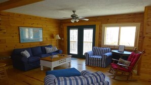 Ein gemütliches Blockhaushaus-Interieur mit einem blauen Sofa, gestreiften Sesseln, einem Schaukelstuhl und Holzdielen.
