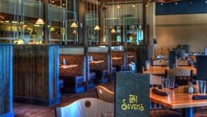 Un interno ristorante con banquette e tavoli, elementi in legno e lampade a sospensione.