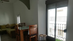 Un coin repas avec une table et des chaises en bois, un petit tabouret et une fenêtre donnant sur un balcon.