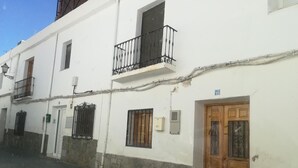 Un bâtiment blanc avec un socle en pierre, une porte en bois et un balcon doté de rampes en métal.