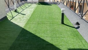 Une terrasse sur le toit, avec un revêtement d’herbe artificielle, un petit espace salon et une vue sur un paysage vallonné.