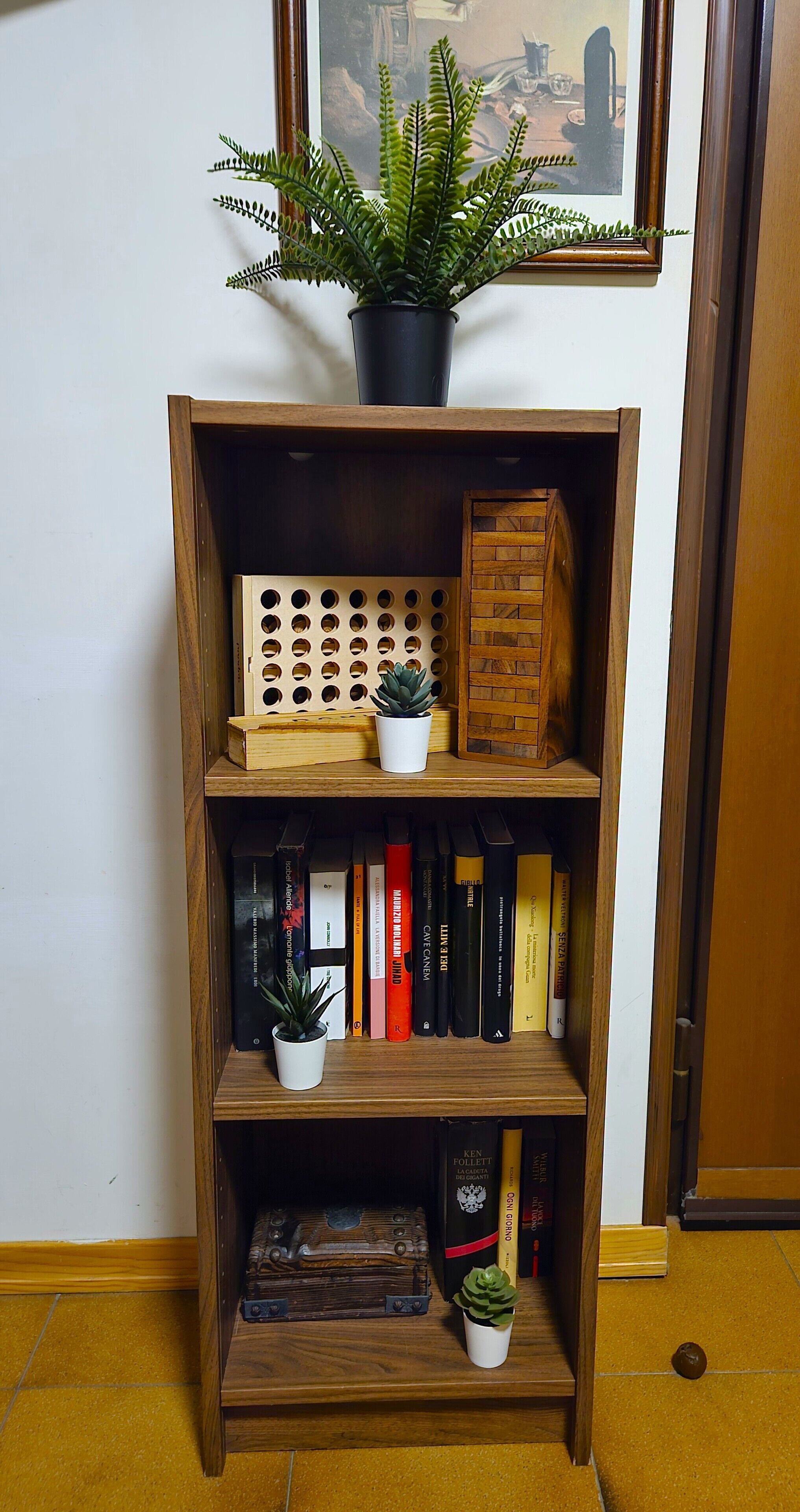 A wooden bookshelf with multiple shelves, some containing books and others with decorative items like a small potted plant and a wooden block.