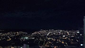 Un paisaje urbano nocturno con edificios iluminados y una colina distante.