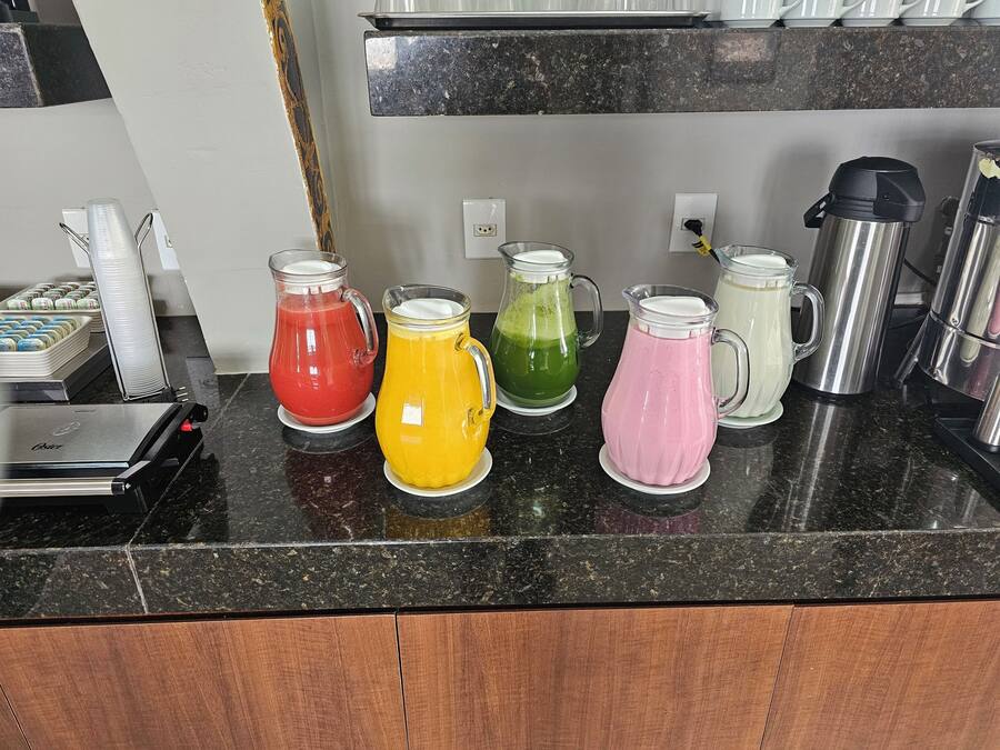 A kitchen counter with five pitchers of colorful beverages and a coffee maker.