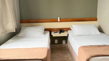 A hotel room with two single beds, a wooden headboard, a small bedside table with a phone, and a curtain on the left.