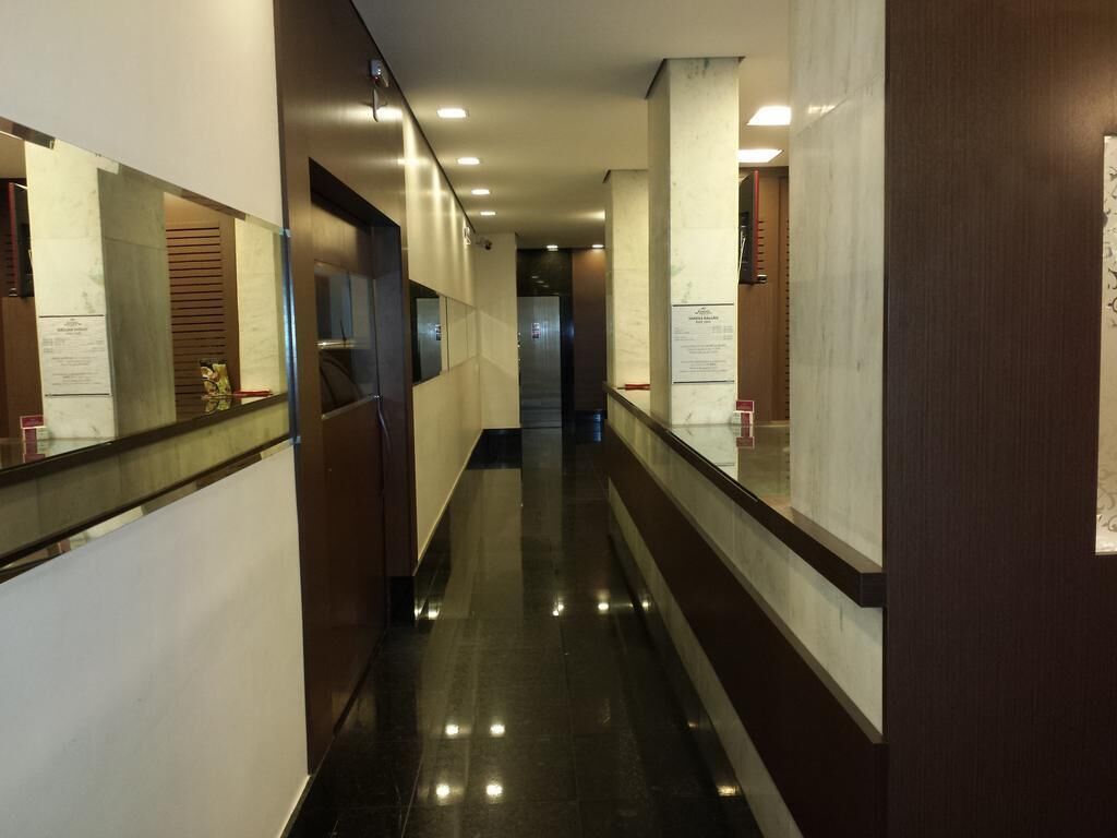 A corridor with reflective floors, wooden paneling, and glass doors leading to rooms.