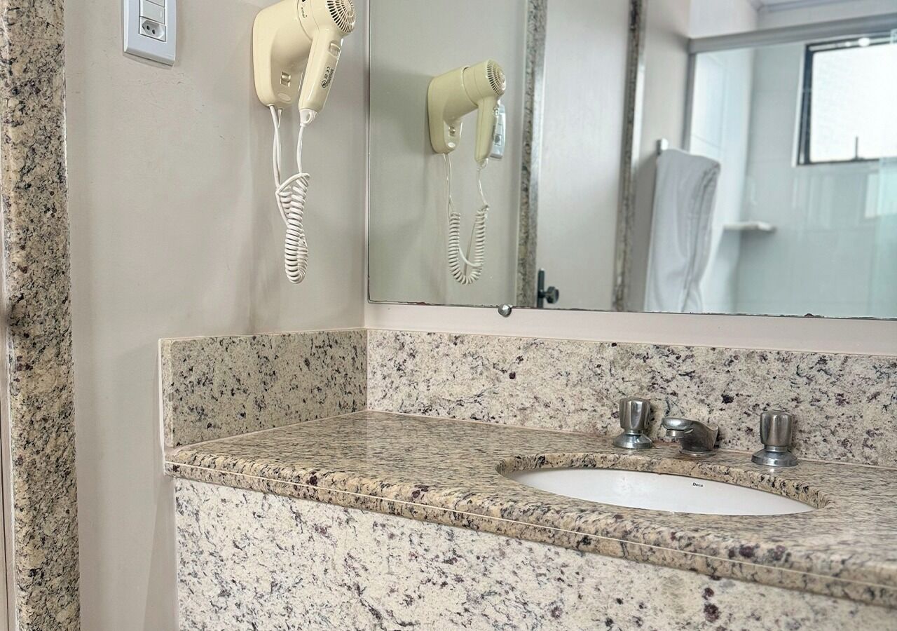 A bathroom with a granite countertop, a sink, and a hairdryer mounted on the wall.