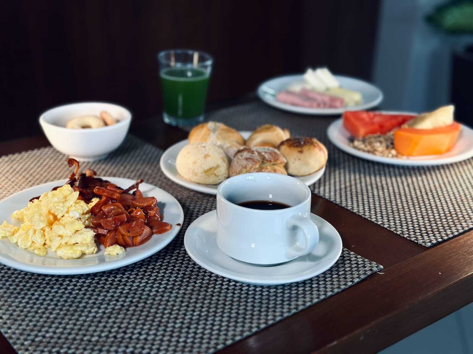 Una mesa de desayuno con huevos revueltos, tocino, pasteles y una taza de café.