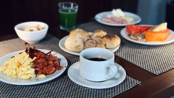 Una mesa de desayuno con huevos revueltos, tocino, pasteles y una taza de café.