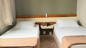 Habitación de hotel con dos camas individuales, una mesita de noche y suelo de madera.
