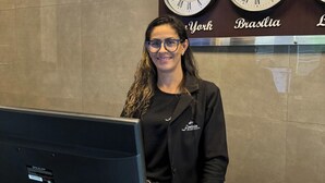 Een receptiebalie met een computer, klokken met de aanduiding 'New York' en 'Brasilia', en een bordje voor 'Fenicia Palace Hotel'.